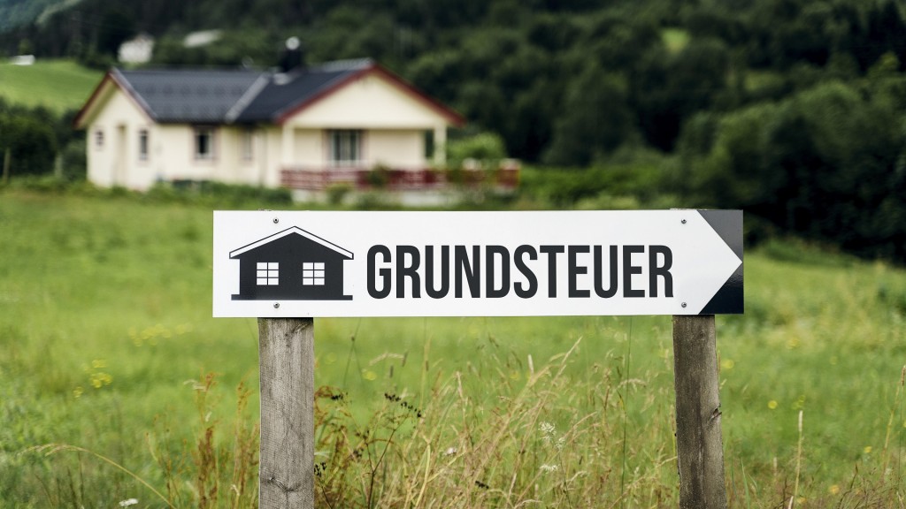 Wegweiser aus Holz in einer Wiese vor einem Haus mit der Aufschrift: Grundsteuer