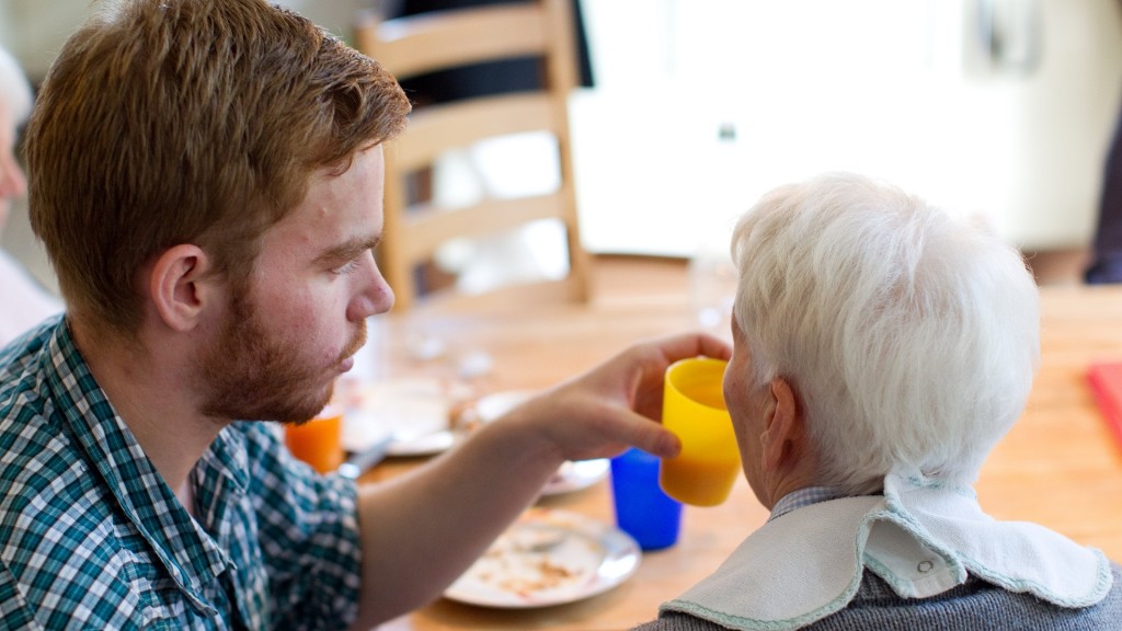 in junger Mann hilft einer Seniorin beim Einnehmen einer Mahlzeit
