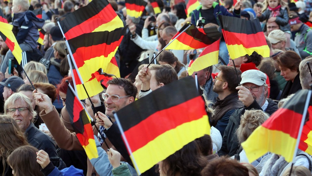 Menschen schwenken am Tag der Deutschen Einheit Nationalfahnen