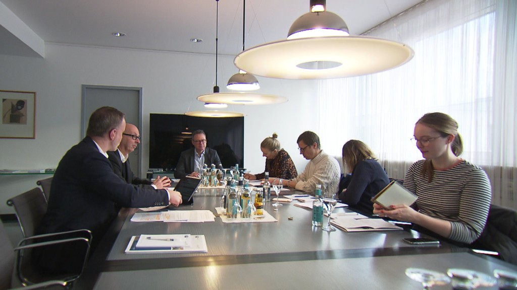 Foto: Menschen sitzen in einem Konferenzsaal an einem Tisch