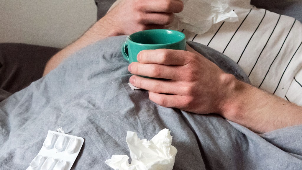 Ein Mann liegt mit Taschentüchern, Teetasse, Nasenspray und Tabletten im Bett