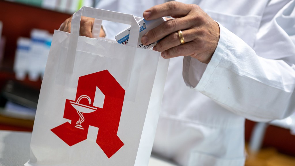 Ein Apotheker legt ein Medikament in eine Papiertasche mit Apotheken-Logo