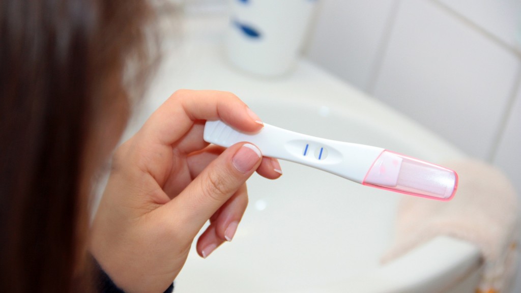 Eine junge Frau blickt auf einen positiven Schwangerschaftstest. 