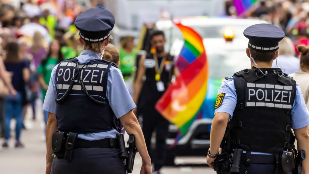 Polizisten im Einsatz bei einer Queer-Veranstaltung, im Hintergrund Teilnehmer mit der sombolischen Regenbogenflagge