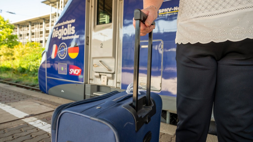 Foto: Eine Reisende steht mit Koffer am Bahnsteig vor einem französischen Regionalzug der SNCF