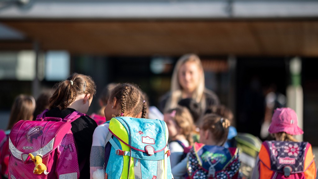 Kinder mit Schulranzen stehen vor einer Grundschule auf dem Hof