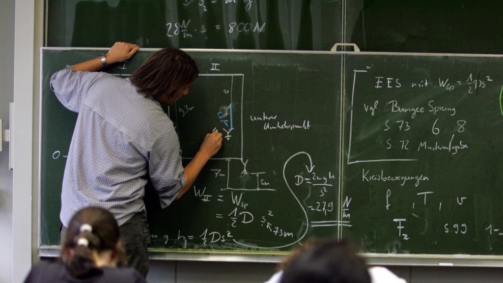 Foto: Ein Lehrer schreibt im Physik-Unterricht Formeln an die Tafel.