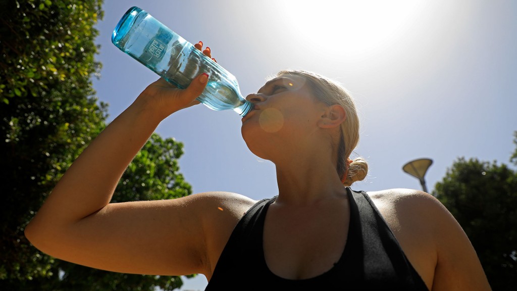 Eine junge Frau trinkt bei prallem Sonnenschein aus einer Wasserflasche