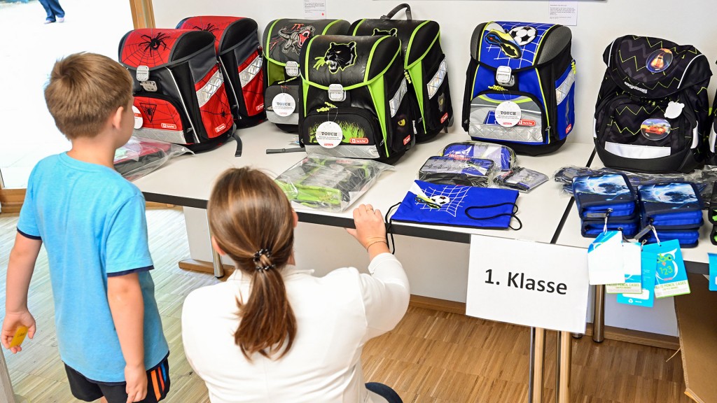 Ein Kind und eine Erwachsene Person vor einer Reihe gut erhaltener gebrauchter Schulranzen