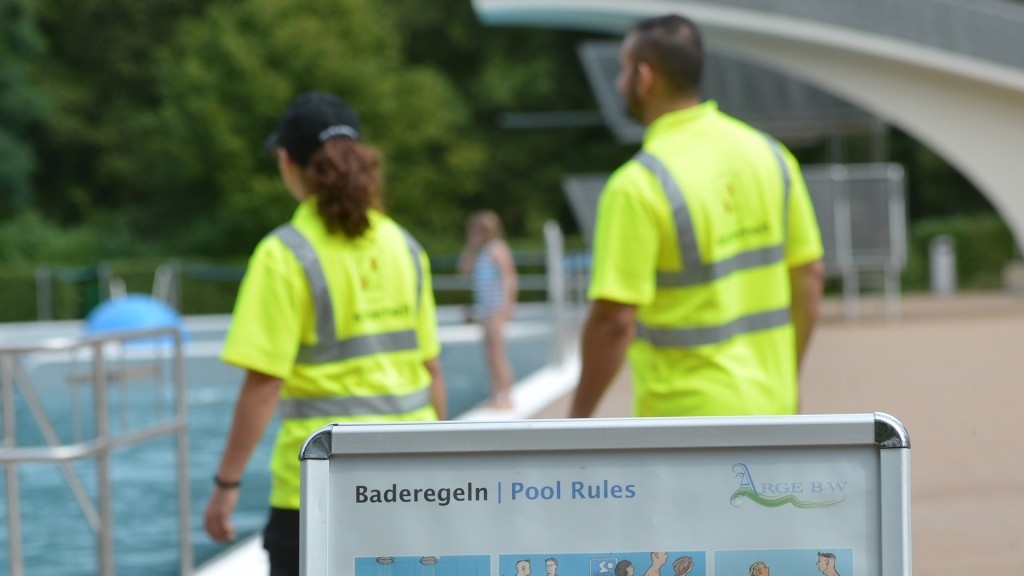 Mitarbeiter eines Sicherheitsdienstes gehen in einem Freibad an einem Schild mit Verhaltensregeln vorbei.