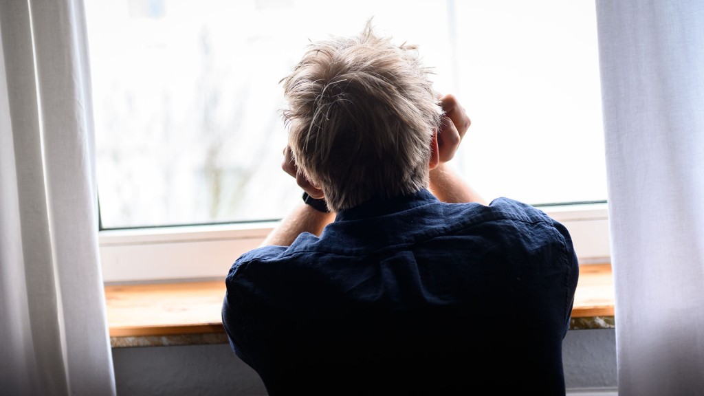 Eine person sitzt mit dem Kopf in die Hände gestützt an einem Fenster