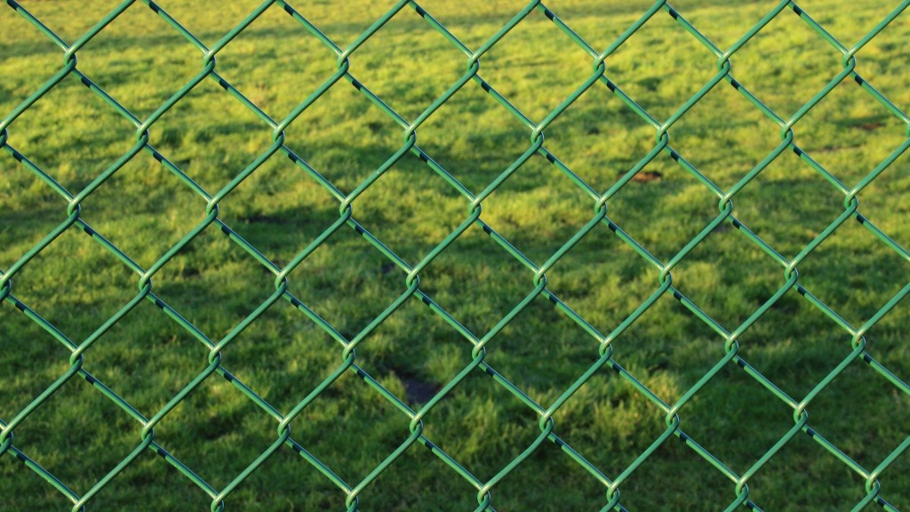 Grüner Maschendrahtzaun mit Wiese im Hintergrund