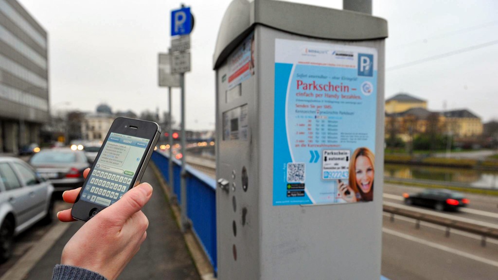 Jemand bucht ein Parkticket mit dem Smartphone vor einem Parkscheinautomat in Saarbrücken