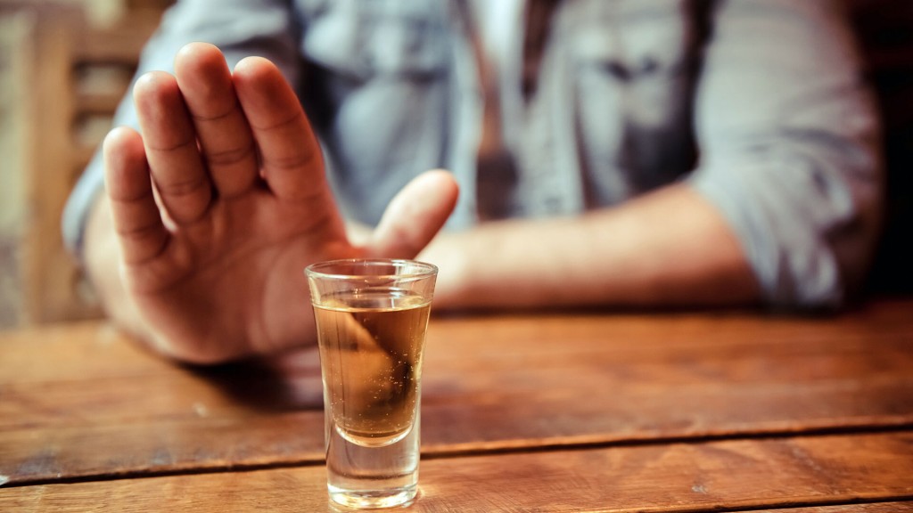 Ein Mann sitzt am Tisch und hält seine Hand ablehnend vor ein alkoholisches Gestränk