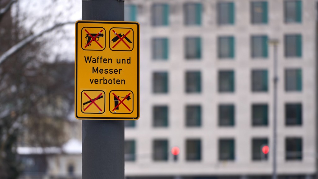 Ein gelbes Schild mit der Aufschrift Waffen und Messer verboten zeigt durchgestrichene Symbole von Pistolen, Messern und anderen Waffen. 