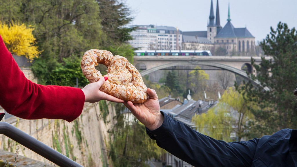 Ein Mann reicht einer Frau eine Brezel vor der Kulisse von Luxemburg