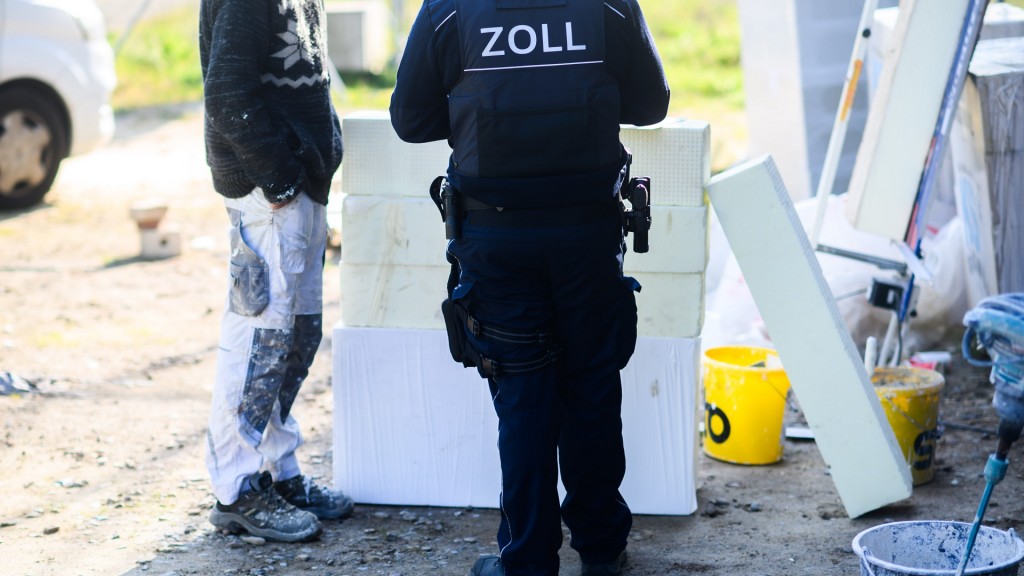 Ein Zollbeamter steht auf einer Baustelle neben einem Bauarbeiter.