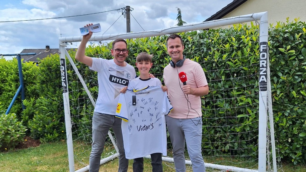 links, Heiko Koch mit den Tickets, in der Mitte Leonard mit dem FCS Trikot mit den Originalunterschriften aus der letzten Saison, rechts SR 1-Moderator Frank Falkenauer