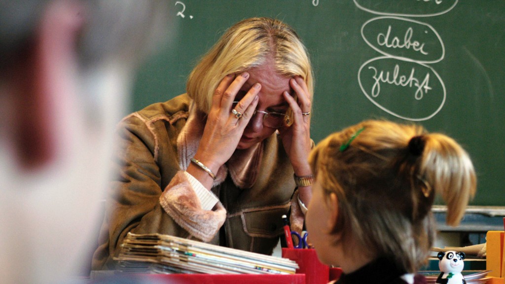 Foto: Eine Lehrerin stützt am Pult den Kopf auf die Hände
