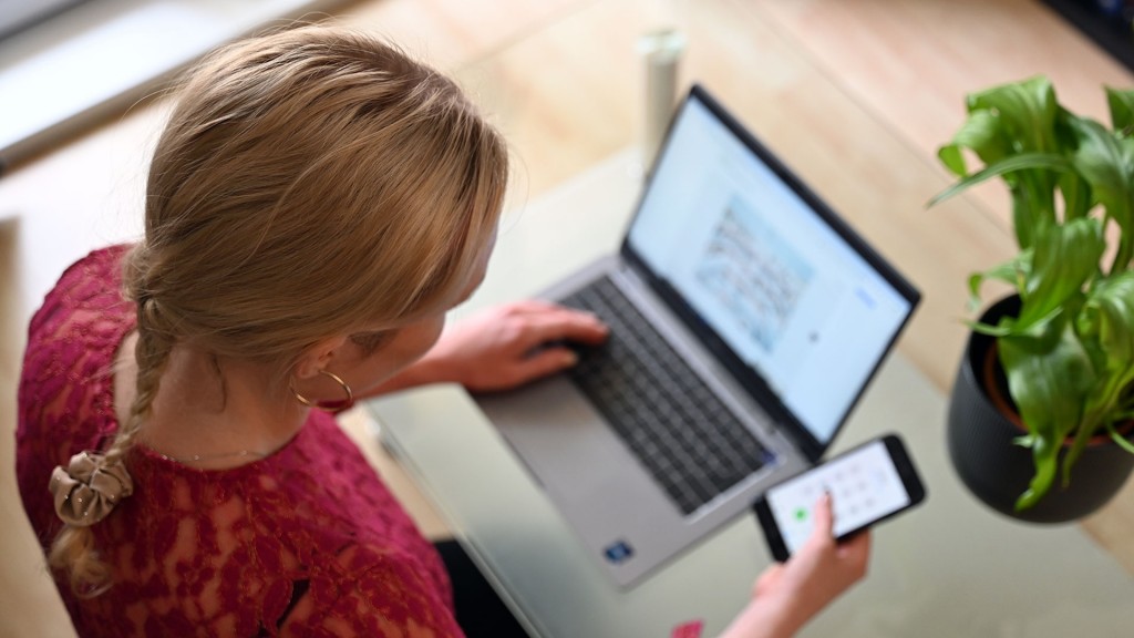 Eine Frau sitzt mit ihrem Smartphone vor einem Laptop