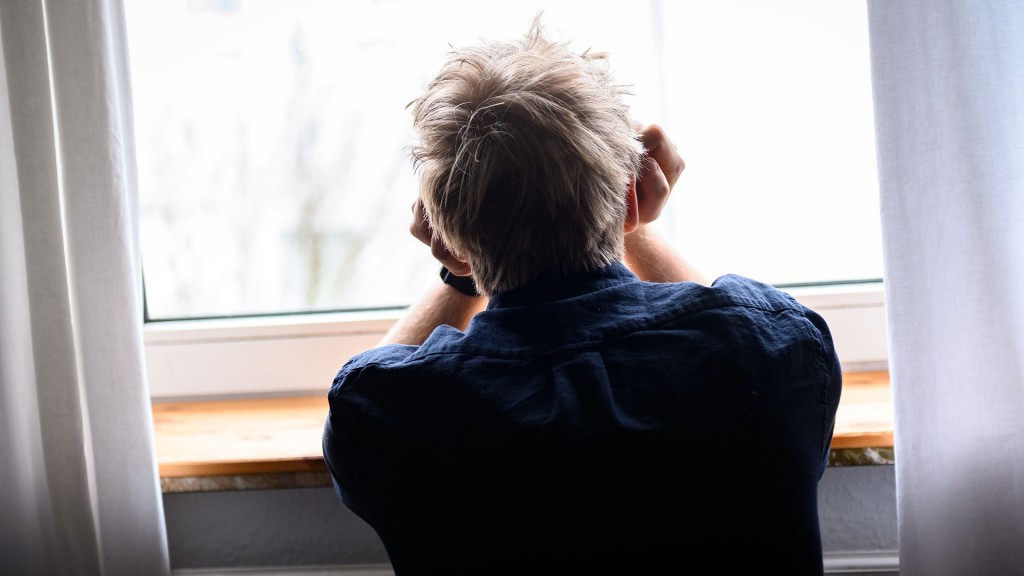 Eine Person sitzt mit dem Kopf in die Hände gestützt an einem Fenster