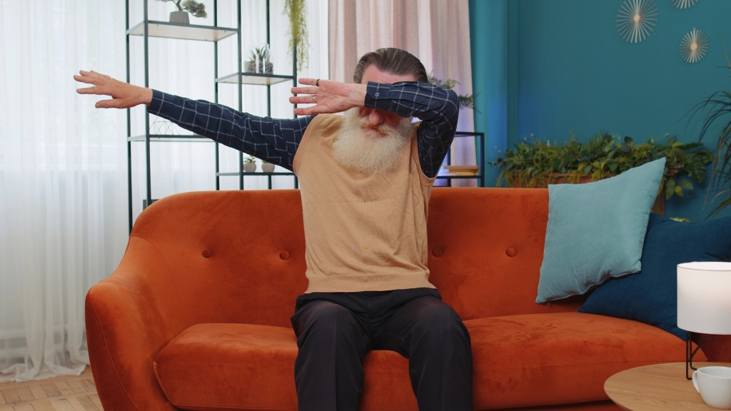 Ein älterer Mann sitzt auf einem Sofa und hat beide Arme in die Luft gehoben, als würde er tanzen.