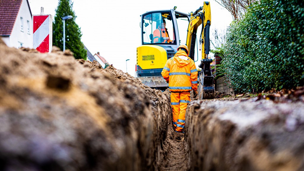 Arbeiter sind mit Bagger und Spaten an einer Straße mit der Erdverlegung von Glasfaserkabeln beschäftigt.
