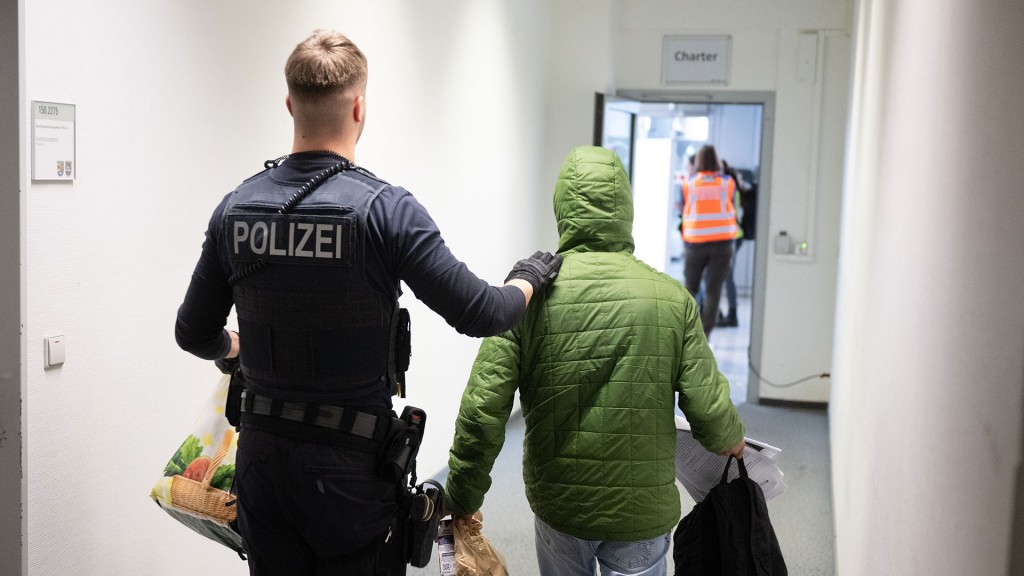 Foto: Ein Polizist läuft mit einem jungen Mann einen Flur entlang.