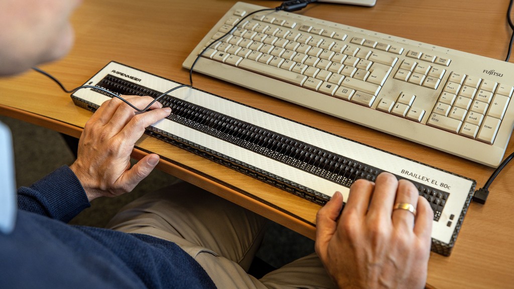 Jemand sitzt an einem Computer-Arbeitspatz mit einer Blindentastatur, die haptisch ertastbare Braille-Schrift ausgibt