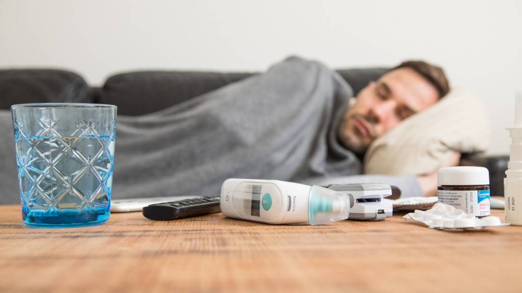 Ein Mann liegt krank auf einem Sofa, vor ihm auf dem Tisch Medikamente und ein Thermometer.