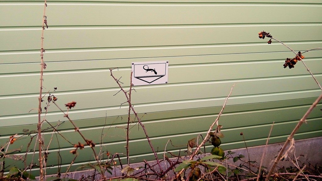 Ein Schild mit einem Lurch weist auf einen Kleintierdurchgang der Lärmschutzwand einer Bahnstrecke hin