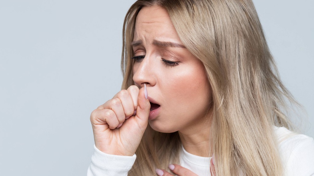 Eine junge Frau hustet sich in die Hand
