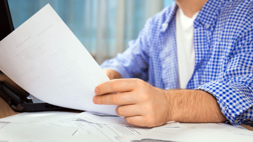 Jemand sitzt am Schreibtisch und hält ein Blatt Papier in der Hand