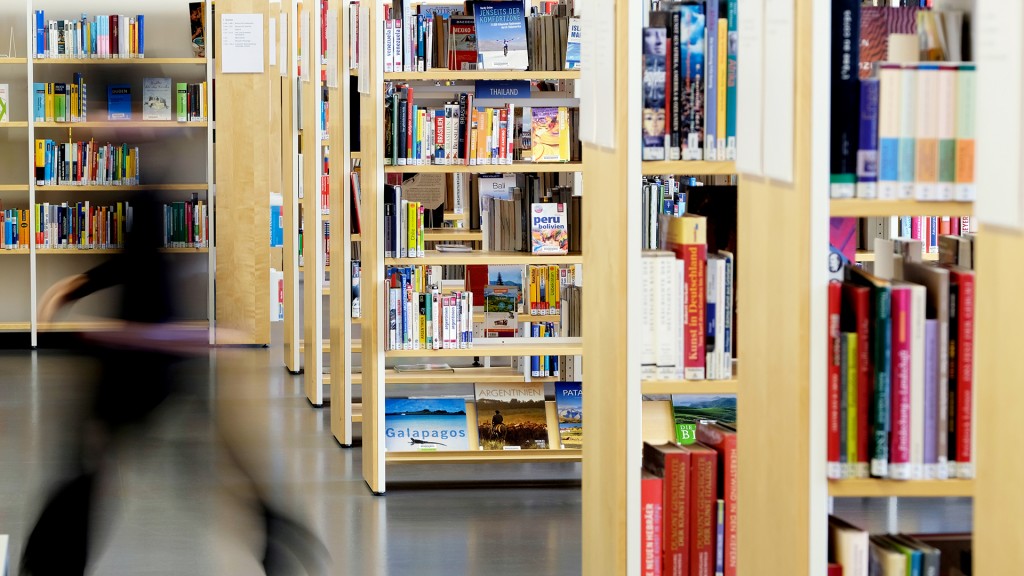 Mitarbeiterin einer Bibliothek geht an Bücherregalen vorbei