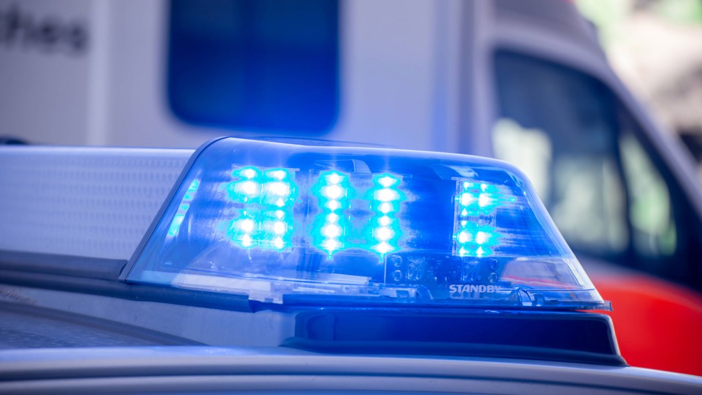 Foto: Nahaufnahme von blinkendem Blaulicht bei einem Polizeieinsatz mit Rettungswagen im Hintergrund    