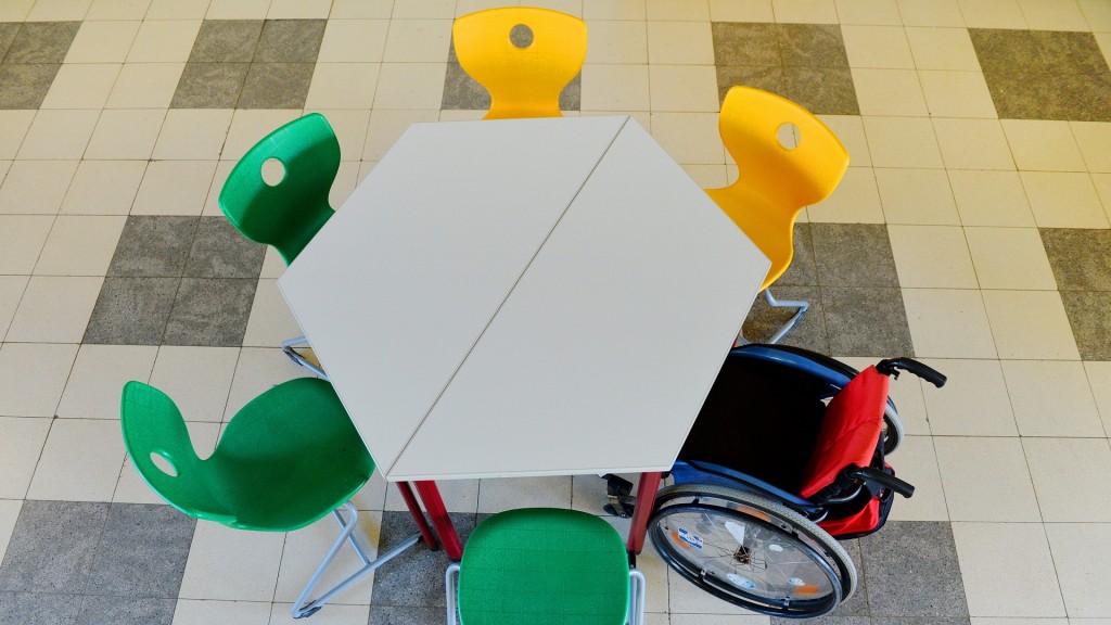 Rollstuhl steht in der Kantine am Tisch zwischen anderen Stühlen