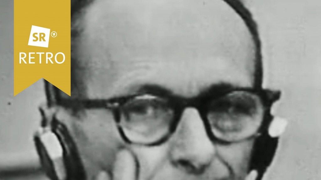 Adolf Eichmann im Gerichtssaal mit Kopfhörern. Er stützt sein Gesicht auf seine Hand.