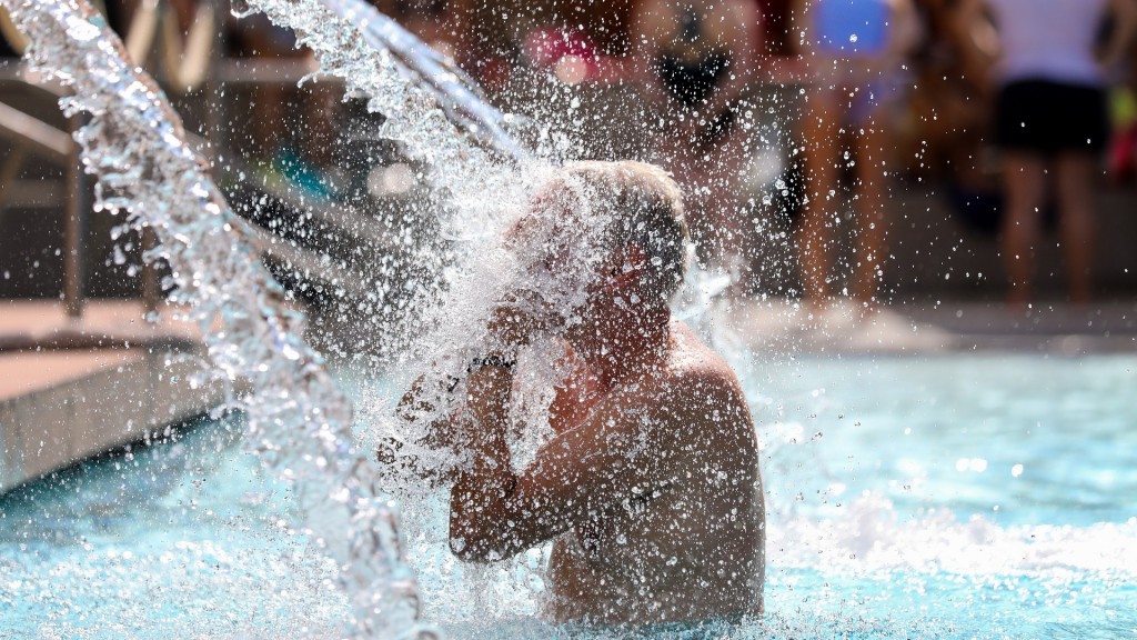 Ein Mann erfrischt sich in einem Freibad unter einer Wasserfontäne.