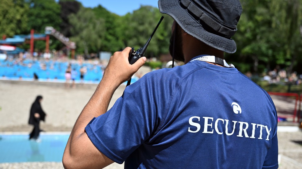 Ein Sicherheitsmitarbeiter steht mit Funkgerät in einem gut besuchten Freibad