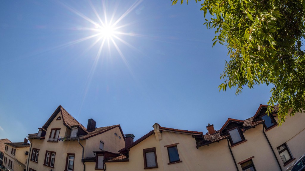 Die Sonne steht hoch über Wohnhäusern am wolkenfreien Himmel