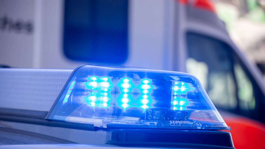 Foto:Nahaufnahme von blinkendem Blaulicht bei einem Polizeieinsatz mit Rettungswagen im Hintergrund    