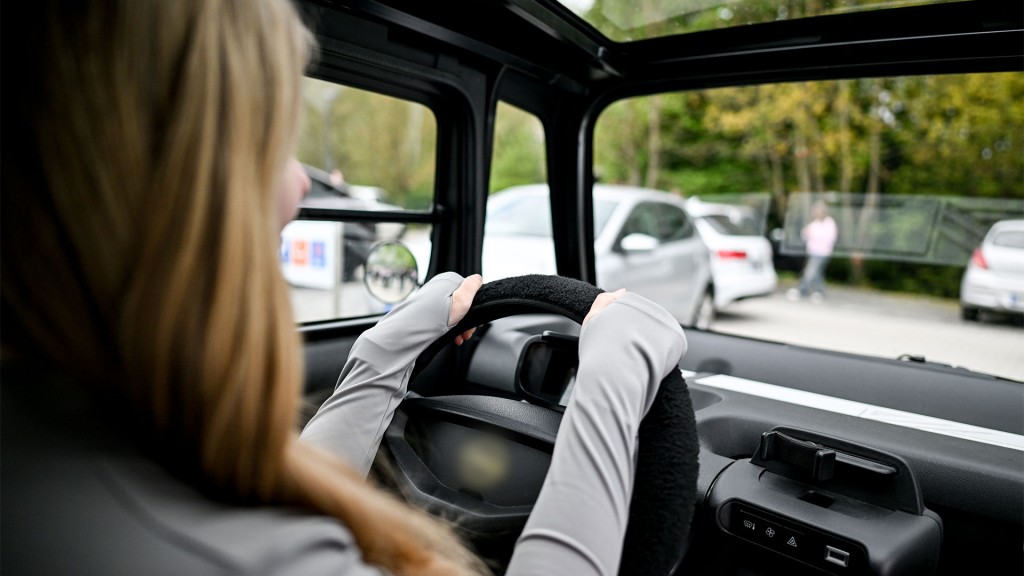 Eine schülerin sitzt im Microcar auf dem Parkplatz und hat die Hände am Lenkrad