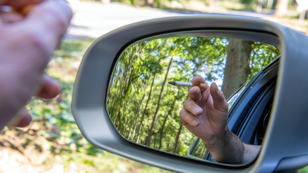 Eine Zigarette wird auf einem Waldparkplatz aus einem Auto gehalten