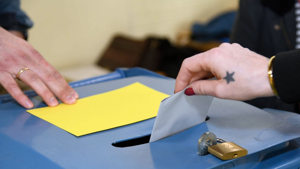 Ein Stimmzettel wird in die Wahlurne eingeworfen