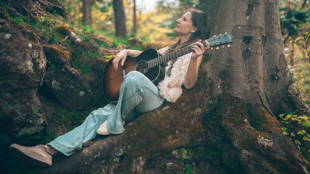 Musikerin Marie Cheyenne lehnt mit der Gitarre im Schoß an einen Baum.