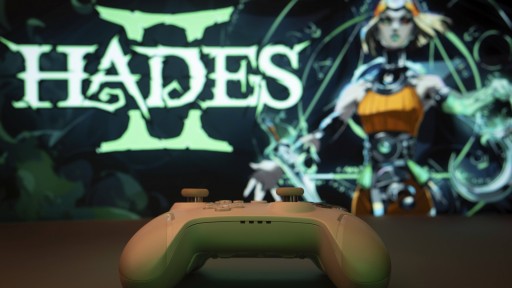 Nahaufnahme eines weißen Gamepads mit dem Hades II auf dem Bildschirm im Hintergrund 